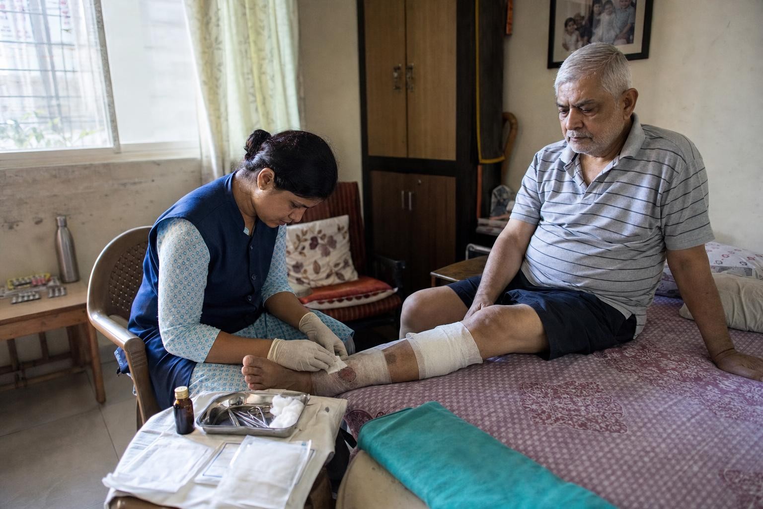 A dressing tray with sterile gauze, gloves and antiseptic laid out on a stool beside a bed
